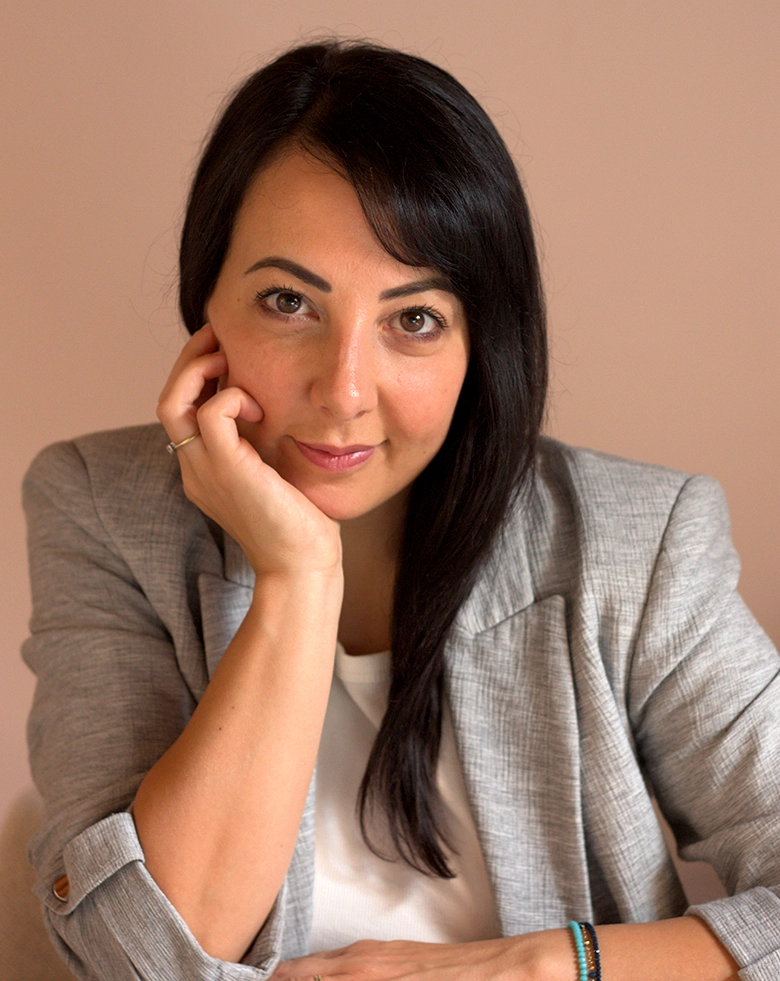 Primo piano professionale di Romina Schipano, titolare di Aiutarelazioni, sorridente in giacca grigia con la mano sul viso, per la pagina di presentazione o la home del sito.