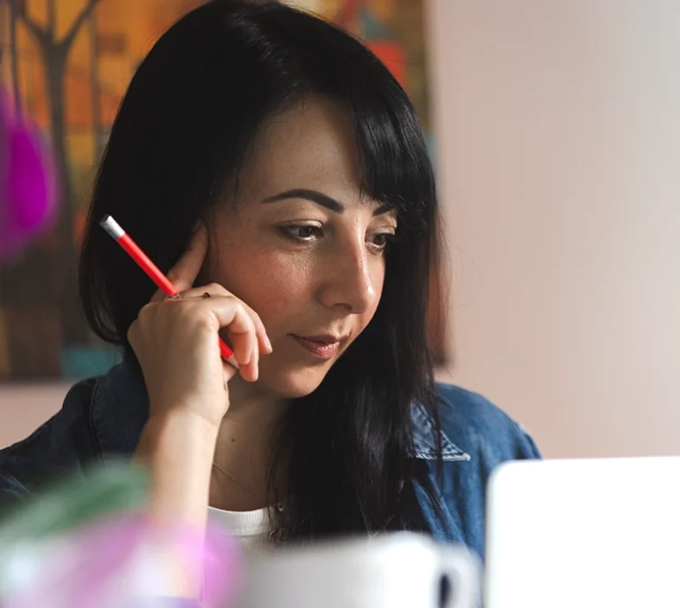 Profilo di Romina Schipano concentrata mentre lavora al computer nel suo studio tenendo una matita rossa