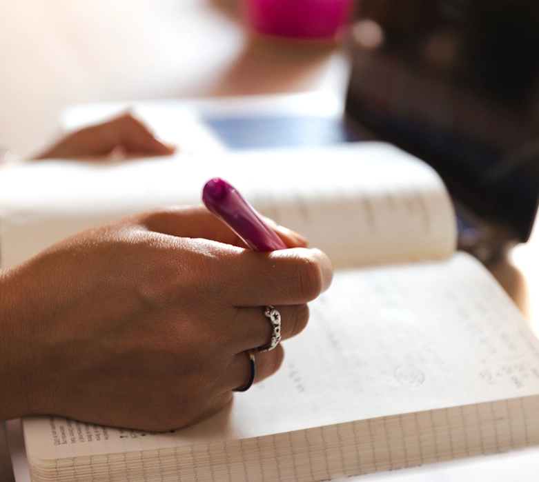 Primo piano delle mani di Romina Schipano mentre prende appunti con una penna fucsia su un quaderno durante una consulenza nel suo studio.